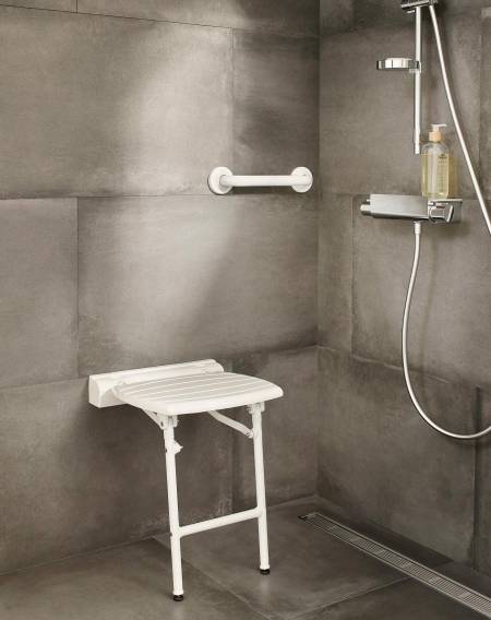 Zona de ducha, con un asiento de ducha abatible con un asidero fijado a la pared y la grifería de ducha a la derecha.. Acceso a la galería. Abre nueva ventana